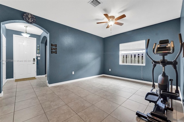 exercise area featuring arched walkways, light tile patterned floors, visible vents, ceiling fan, and baseboards