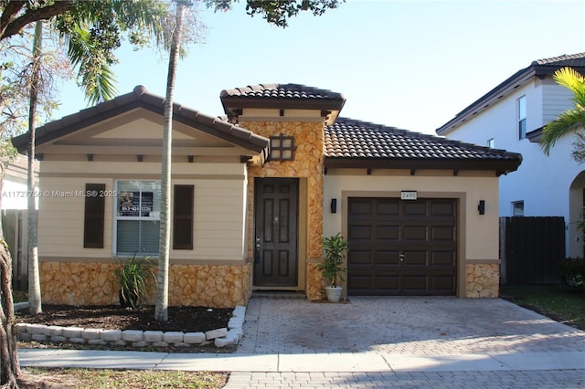 mediterranean / spanish house with a garage, stone siding, and a tiled roof