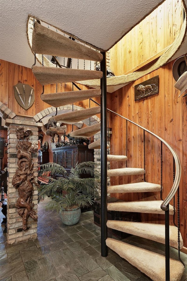 stairs featuring a textured ceiling and wood walls