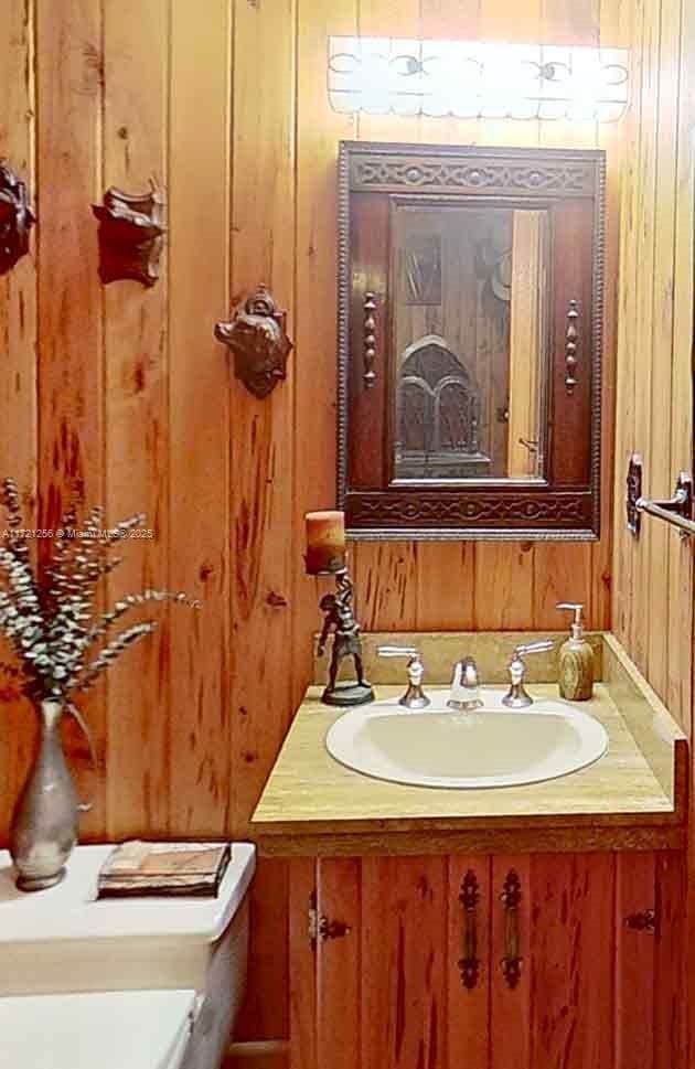 bathroom with vanity, toilet, and wood walls