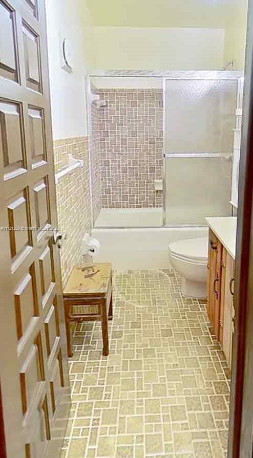 full bathroom with vanity, tile walls, shower / bath combination with glass door, and toilet