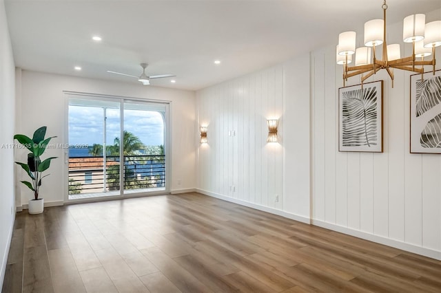 unfurnished room with ceiling fan with notable chandelier and wood-type flooring