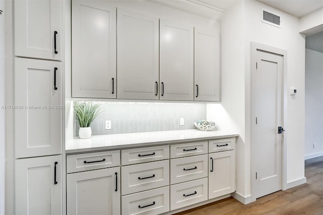 bar featuring decorative backsplash, white cabinetry, and light hardwood / wood-style floors