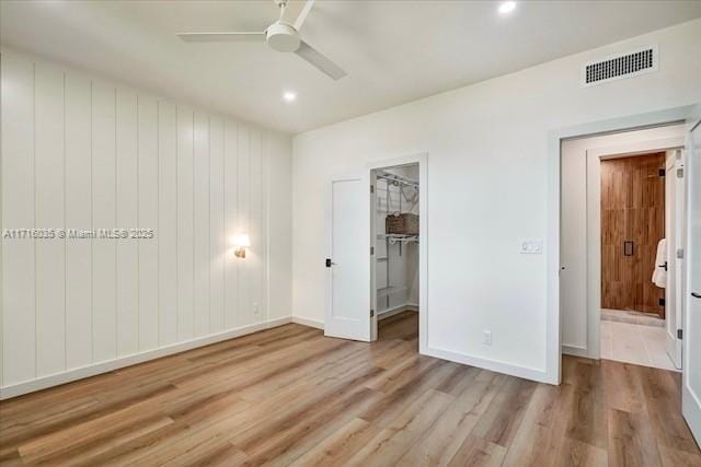 unfurnished bedroom featuring ceiling fan, a closet, a walk in closet, and light wood-type flooring