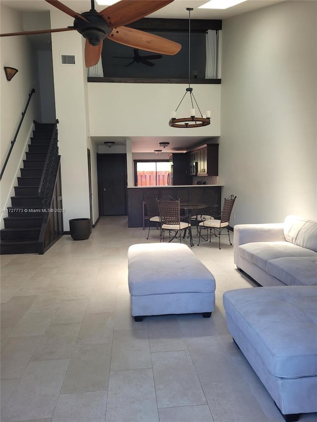 living room with a towering ceiling, visible vents, and ceiling fan