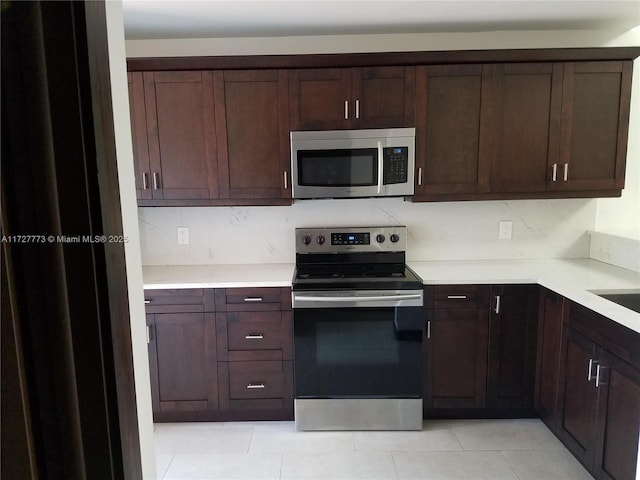 kitchen with light tile patterned flooring, appliances with stainless steel finishes, dark brown cabinets, and backsplash