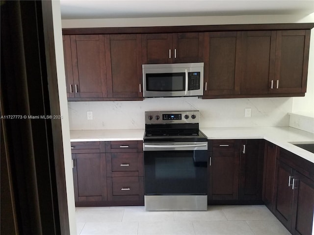 kitchen featuring dark brown cabinetry, stainless steel appliances, light tile patterned flooring, and light countertops