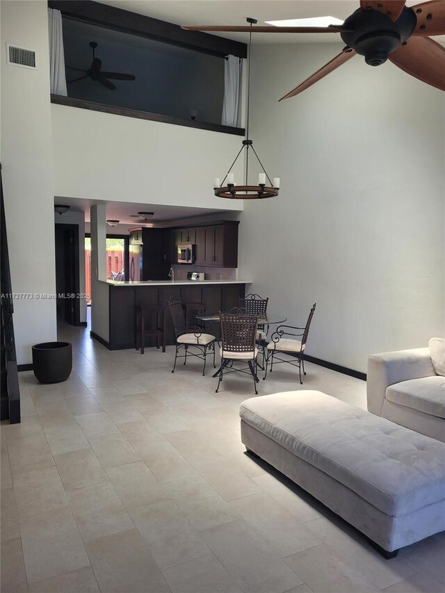 living room with ceiling fan with notable chandelier, a towering ceiling, and visible vents
