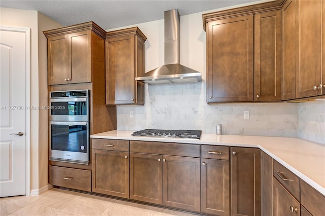 kitchen with light tile patterned floors, stainless steel appliances, decorative backsplash, a textured ceiling, and wall chimney exhaust hood