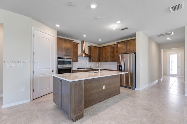 kitchen featuring light tile patterned floors, a center island with sink, stainless steel appliances, wall chimney exhaust hood, and sink