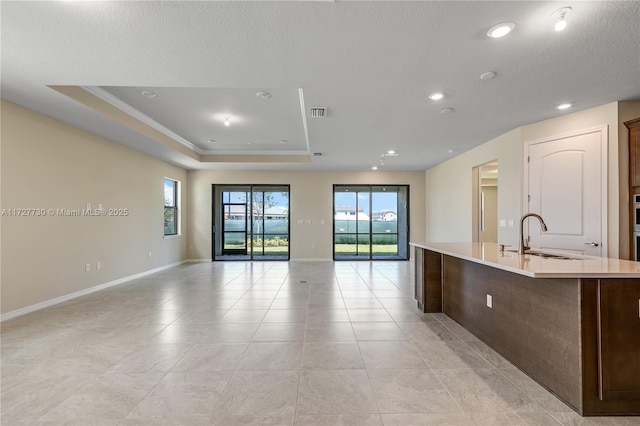 kitchen with a healthy amount of sunlight, sink, an island with sink, and a tray ceiling