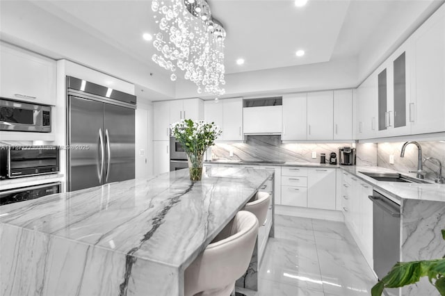 kitchen with light stone countertops, a spacious island, white cabinetry, built in appliances, and sink