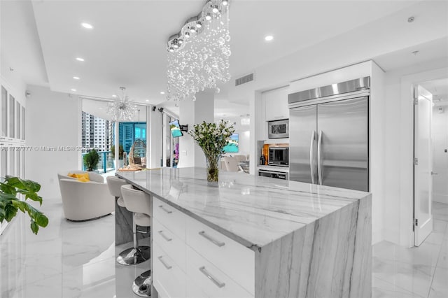 kitchen with light stone countertops, white cabinets, stainless steel appliances, a large island, and a breakfast bar