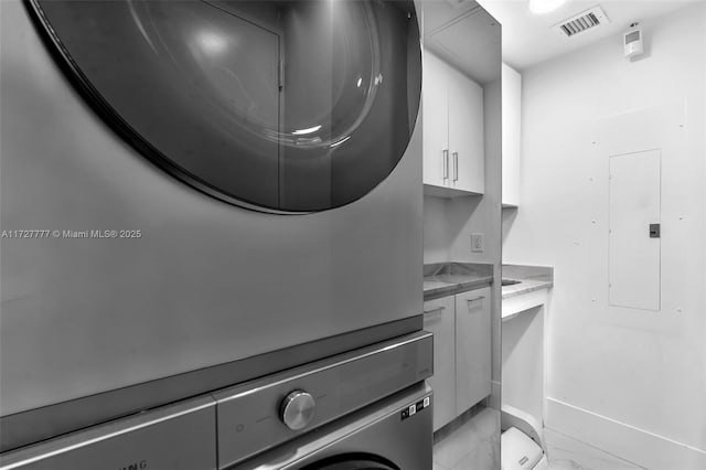 laundry room featuring stacked washing maching and dryer, cabinets, and electric panel