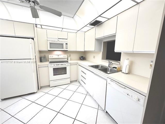 kitchen with white appliances, white cabinetry, light tile patterned floors, sink, and ceiling fan