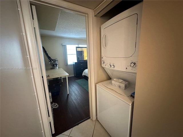 clothes washing area with a textured ceiling, light tile patterned floors, and stacked washing maching and dryer