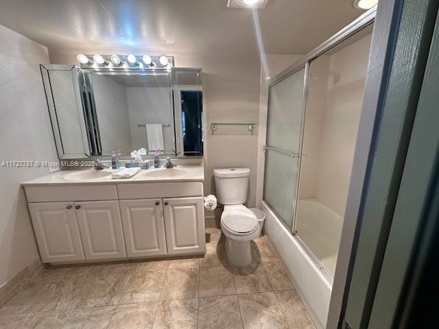 bathroom featuring double vanity, bath / shower combo with glass door, toilet, and a sink