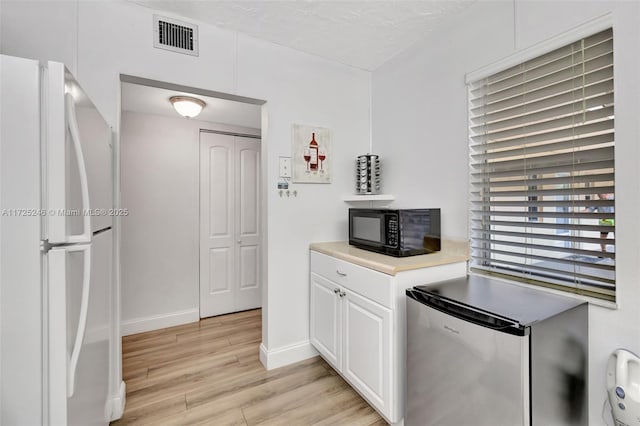 kitchen with a textured ceiling, white cabinetry, white refrigerator, stainless steel fridge, and light wood-type flooring