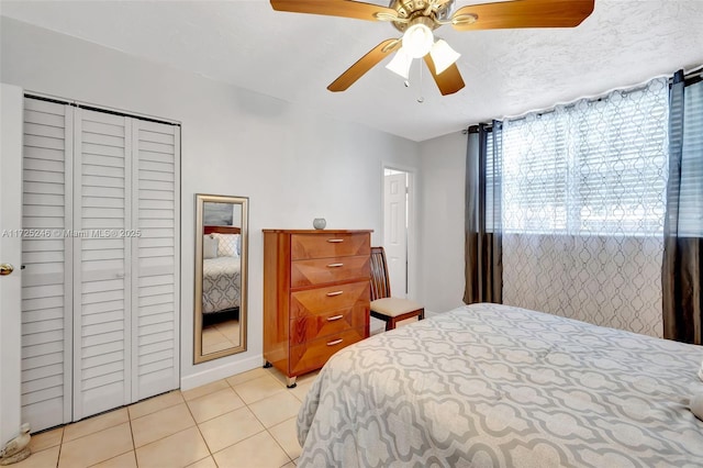 bedroom with ceiling fan, light tile patterned floors, a closet, and a textured ceiling