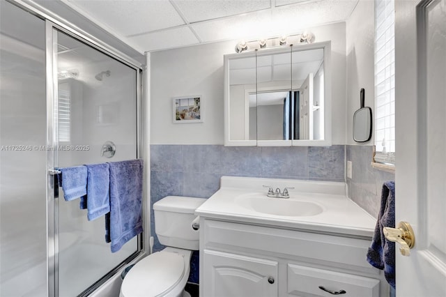 bathroom featuring toilet, tile walls, walk in shower, a drop ceiling, and vanity