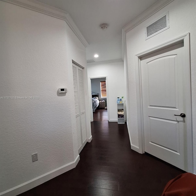 corridor with dark wood-style floors, baseboards, visible vents, ornamental molding, and a textured wall