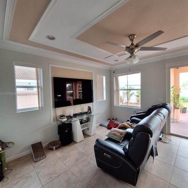 living area featuring ceiling fan, baseboards, a tray ceiling, ornamental molding, and light tile patterned floors