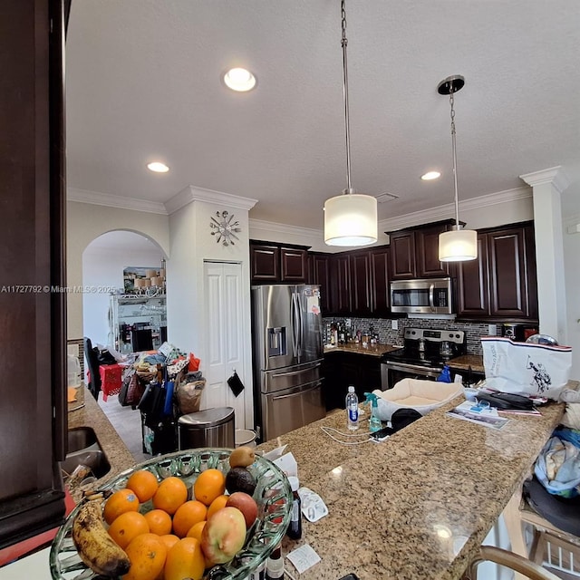 kitchen featuring light stone countertops, arched walkways, dark brown cabinetry, appliances with stainless steel finishes, and backsplash