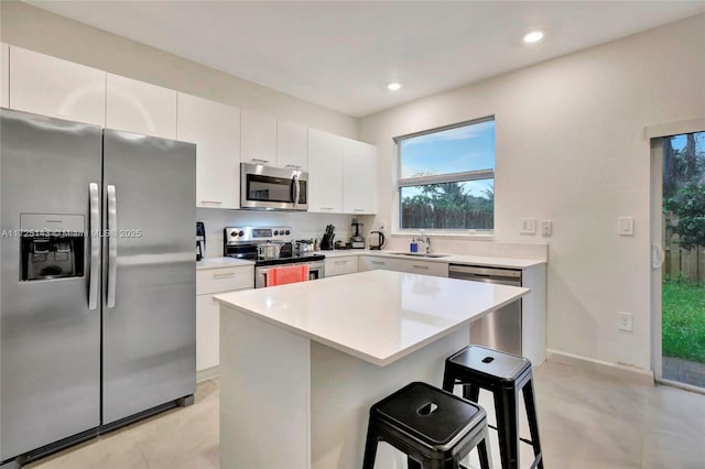 kitchen featuring white cabinets, appliances with stainless steel finishes, a kitchen island, sink, and a breakfast bar area