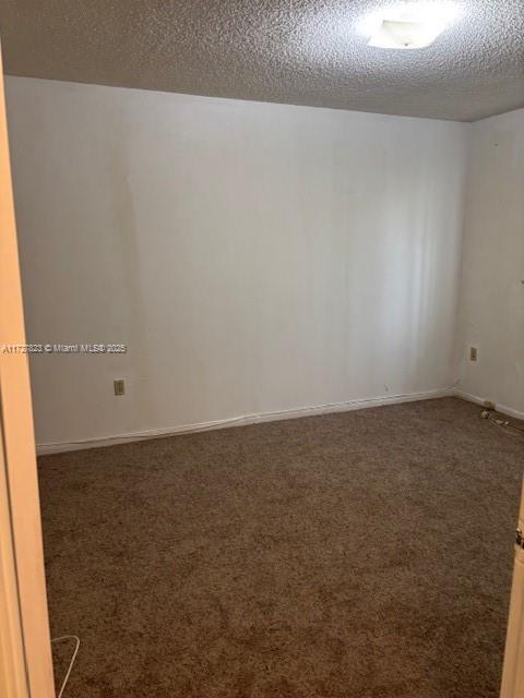 spare room featuring a textured ceiling and dark carpet