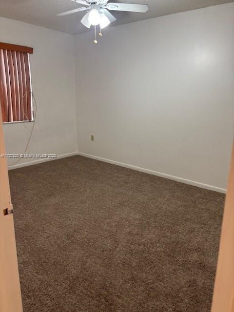 spare room featuring ceiling fan and dark colored carpet