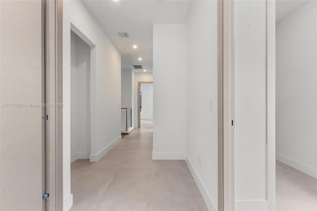 corridor with concrete floors, visible vents, and baseboards