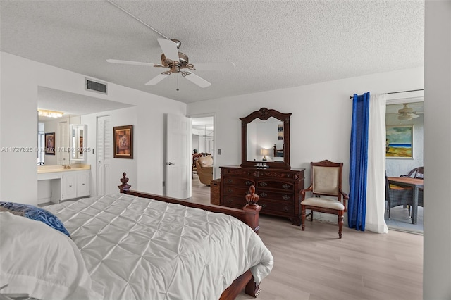 bedroom featuring ceiling fan, ensuite bath, a textured ceiling, and light hardwood / wood-style flooring