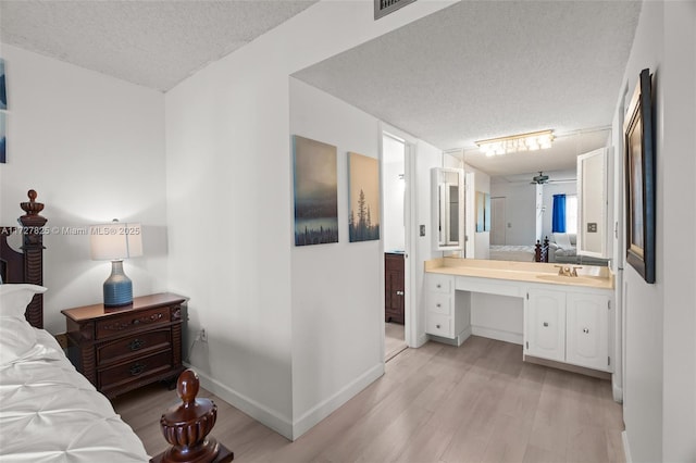 bedroom featuring ensuite bathroom, sink, a textured ceiling, and light hardwood / wood-style floors