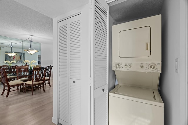 laundry room featuring a textured ceiling, stacked washer / drying machine, and light hardwood / wood-style flooring