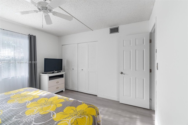 bedroom with ceiling fan, light hardwood / wood-style floors, a textured ceiling, and a closet