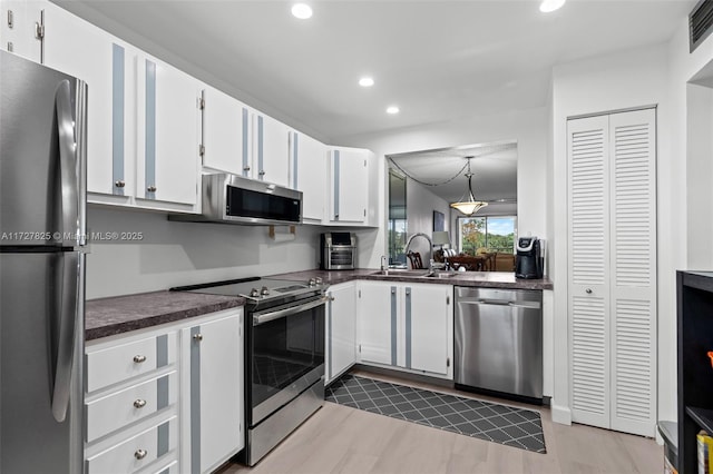 kitchen featuring sink, white cabinetry, hanging light fixtures, light wood-type flooring, and appliances with stainless steel finishes