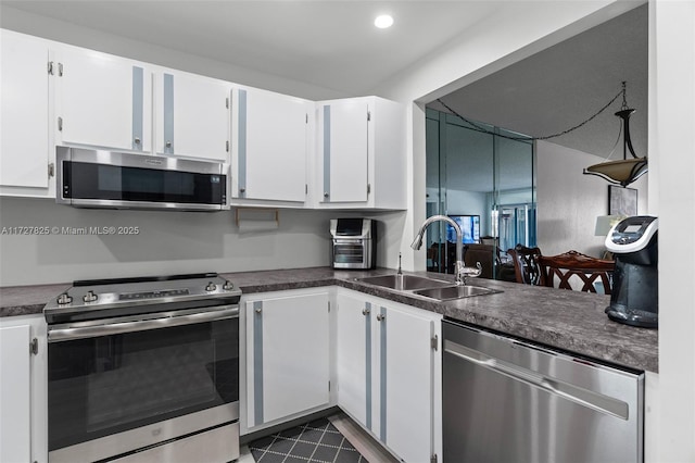 kitchen featuring appliances with stainless steel finishes, dark tile patterned flooring, white cabinets, and sink