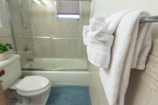 bathroom with toilet and shower / bath combination with glass door