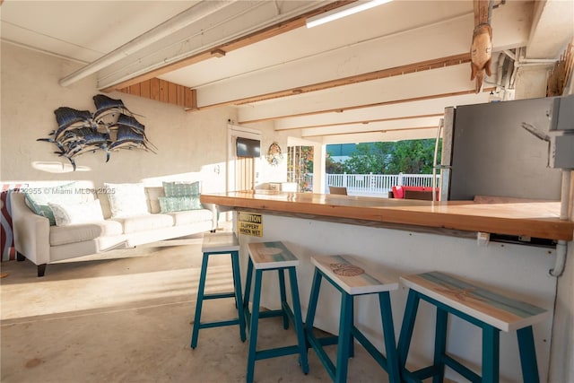 interior space featuring stainless steel fridge, wooden counters, a kitchen breakfast bar, and concrete floors