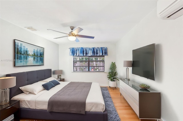 bedroom with light wood-type flooring, ceiling fan, and a wall unit AC