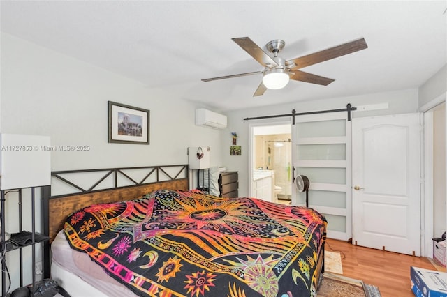 bedroom with ensuite bathroom, light hardwood / wood-style floors, a barn door, ceiling fan, and a wall mounted AC