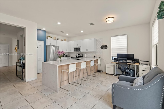 kitchen featuring appliances with stainless steel finishes, white cabinetry, decorative backsplash, a kitchen breakfast bar, and light tile patterned floors