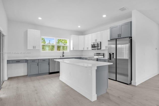 kitchen with a center island, stainless steel appliances, sink, gray cabinets, and light wood-type flooring