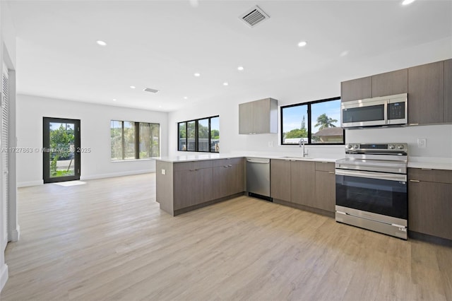 kitchen featuring stainless steel appliances, light hardwood / wood-style flooring, kitchen peninsula, and sink