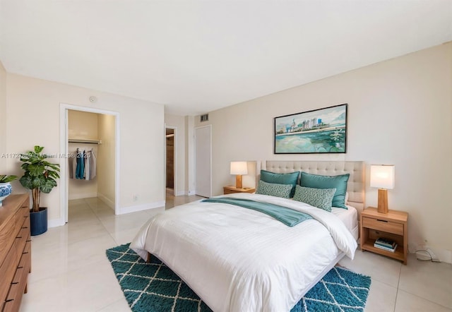 bedroom featuring light tile patterned flooring, visible vents, baseboards, a closet, and a walk in closet