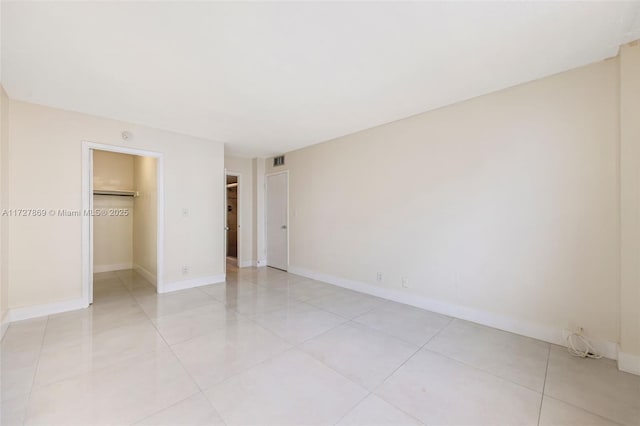 unfurnished bedroom with a walk in closet, a closet, visible vents, light tile patterned flooring, and baseboards