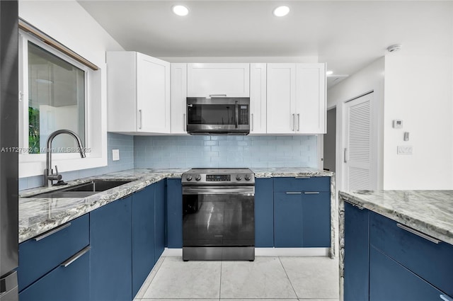 kitchen with sink, white cabinetry, blue cabinetry, stainless steel appliances, and light stone counters