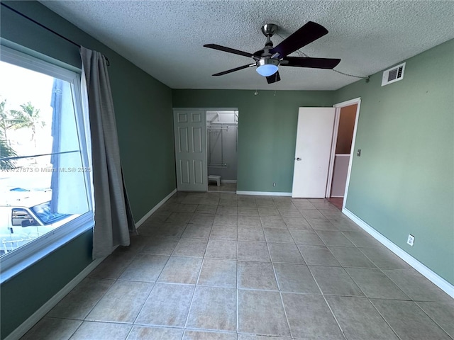 tiled empty room with ceiling fan and a textured ceiling