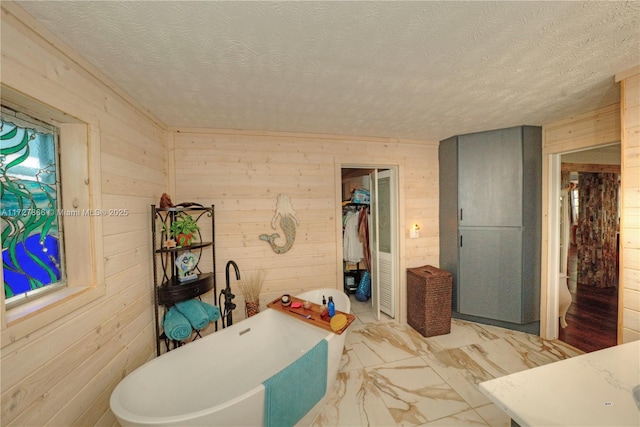 bathroom with a textured ceiling, a tub to relax in, and wood walls