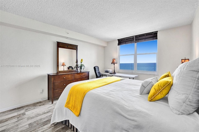 bedroom featuring a textured ceiling, a water view, and hardwood / wood-style floors